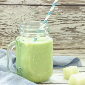 A mason jar glass filled with honeydew smoothie on a wood background.