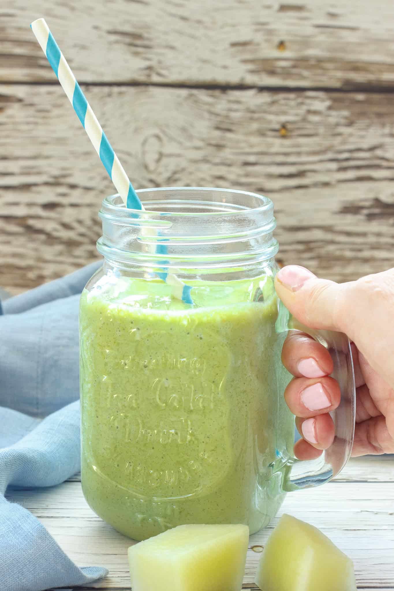 A hand holding a honeydew smoothie in a mason jar glass. 