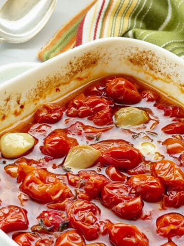 A white casserole dish with slow roasted grape tomatoes and garlic