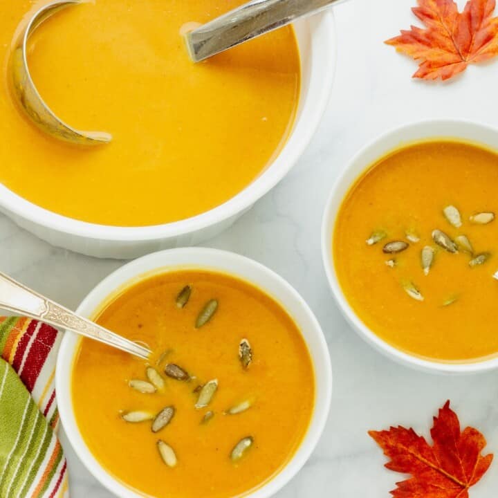 Two white bowls with sweet potato bisque with a large white soup tureen and ladle next to the bowls.