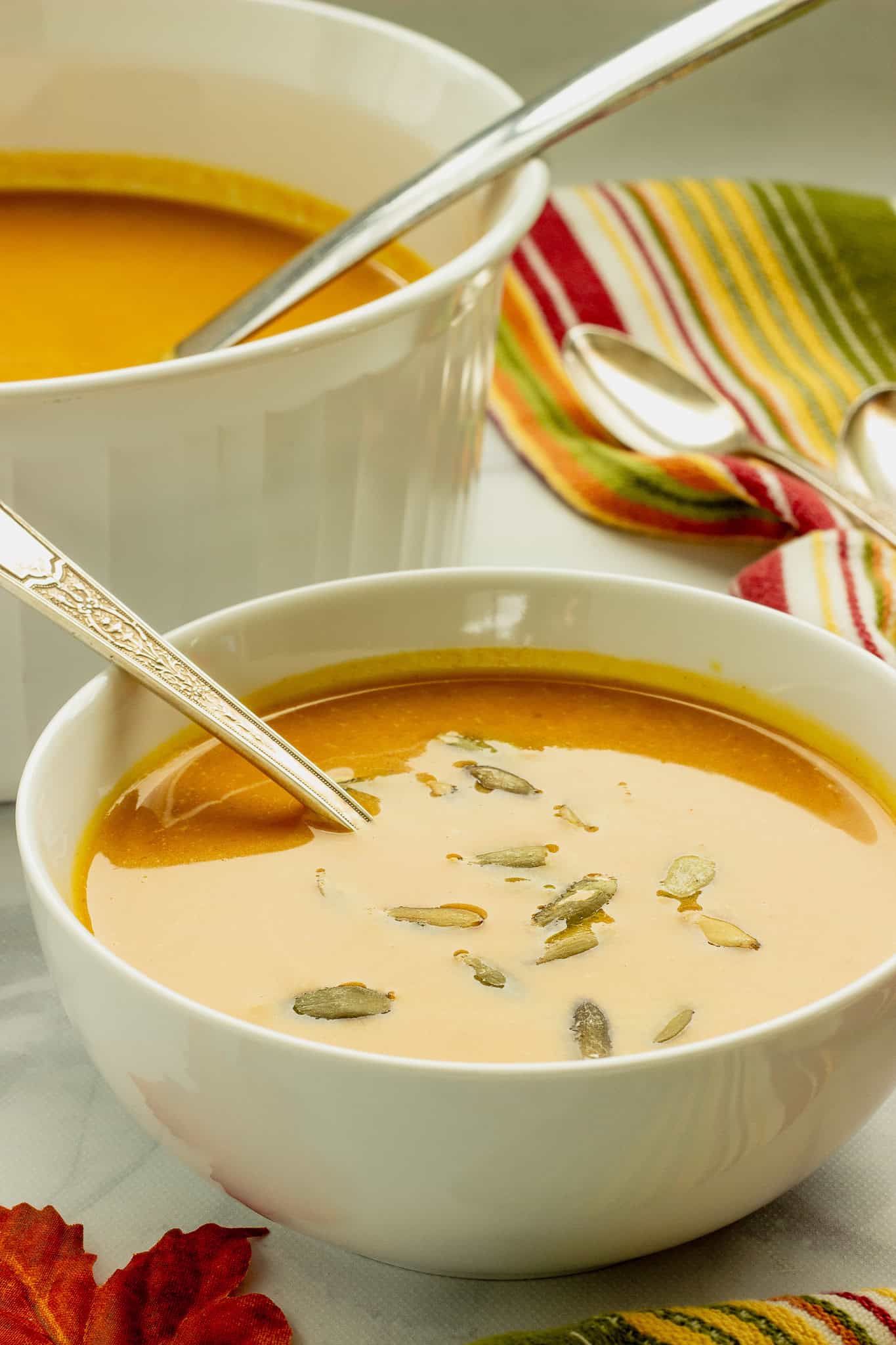 A white bowl of curried sweet potato bisque. A white soup tureen with ladle, and a striped napkin are next to the bowl of soup.
