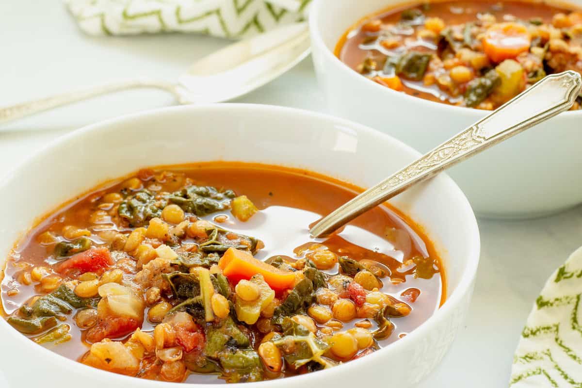A white bowl with sausage and lentil soup and a spoon. A second bowl of soup is in the background.