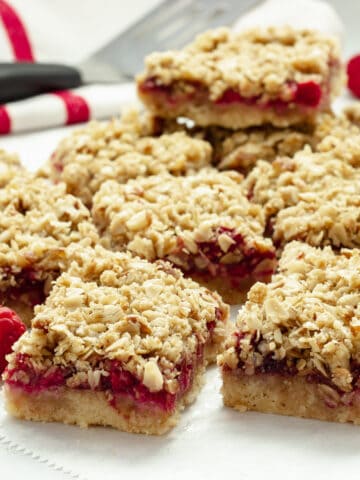 Raspberry oatmeal bars on a sheet of parchment paper with a red and white striped napkin and fresh raspberries in the background.