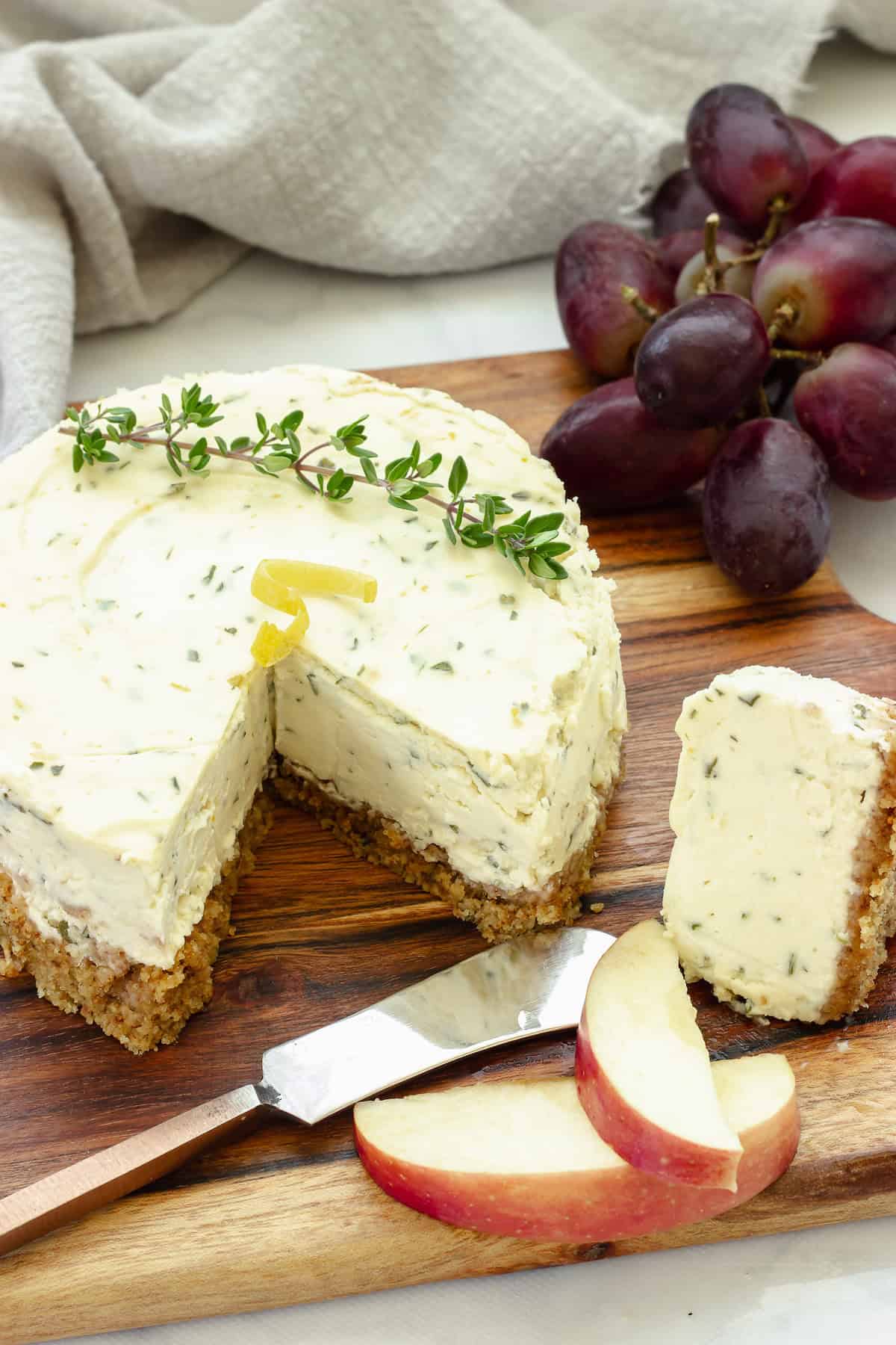 A mini savory cheesecake sitting on a cheeseboard with a piece cut out. Red grapes are in the background.