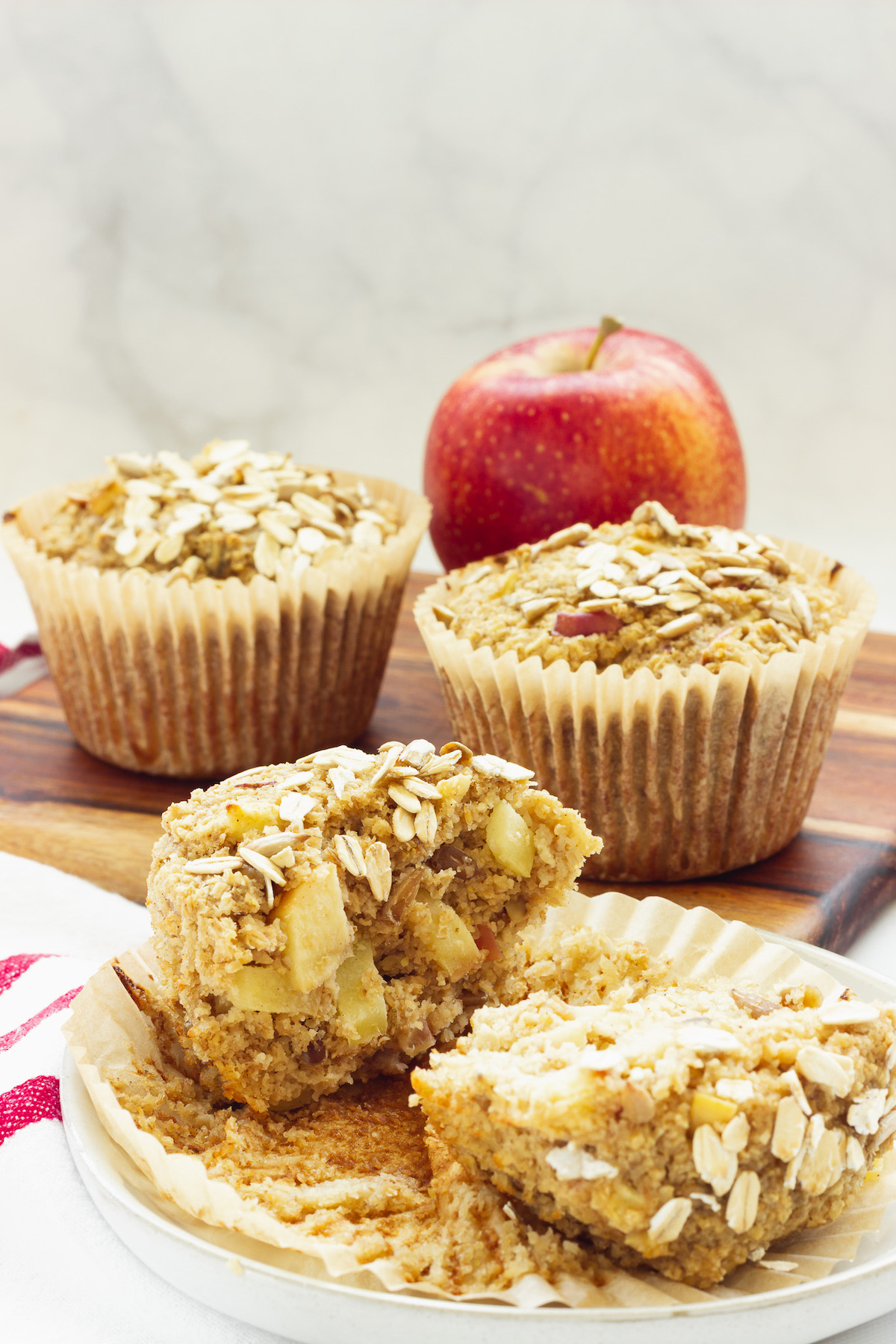 Three oat bran muffins and a red apple. One of the muffins is cut open.