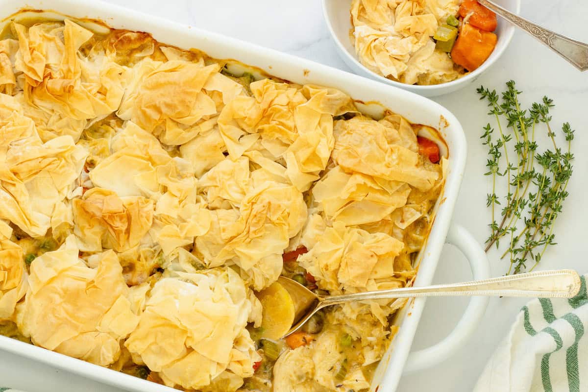 A white, rectangular casserole pan and small white bowl with chicken pot pie casserole on a white background.