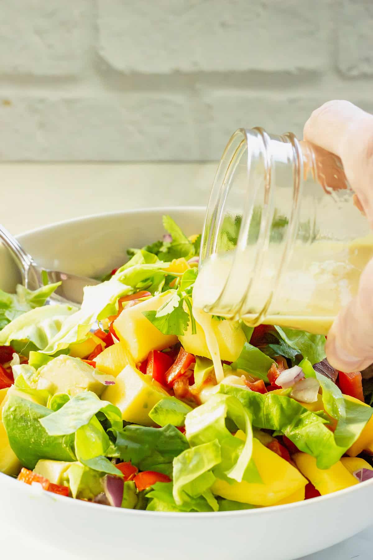 A jar of dressing being poured over a mango avocado salad