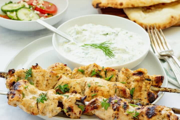 A platter of grilled chicken tzatziki with a bowl of tzatziki sauce behind it.
