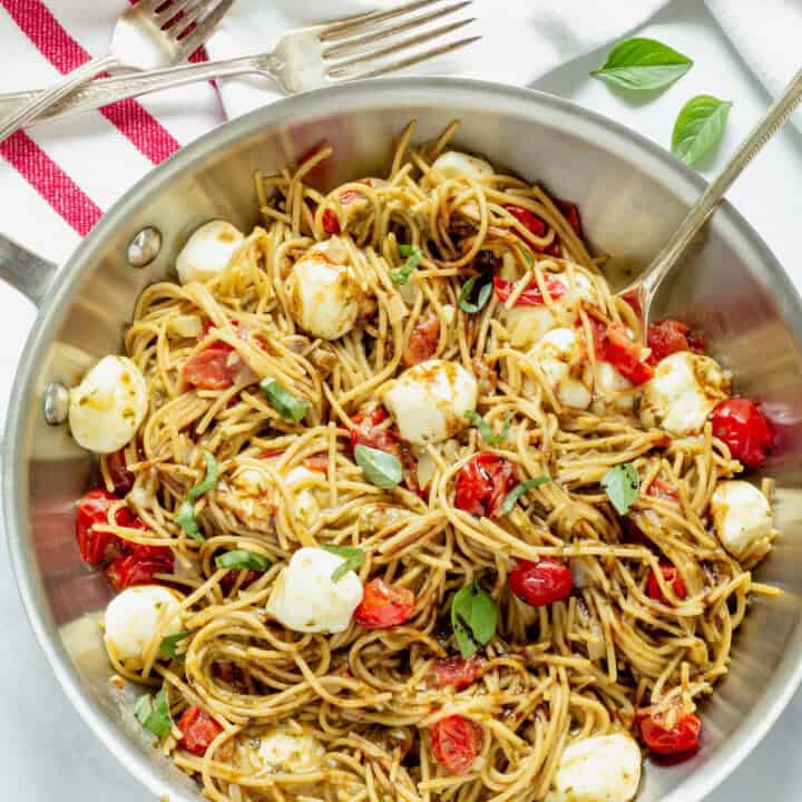 A pan of Caprese pasta with a red and white striped napkin.