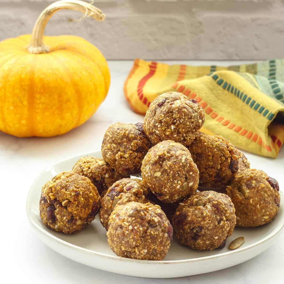 A plate of pumpkin spice protein balls with a small pumpkin and a striped napkin in the background.
