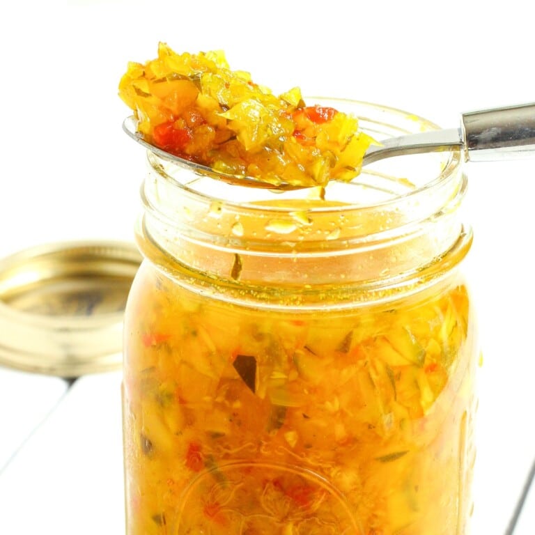A jar of homemade zucchini relish with a spoon of relish over the top of the jar.