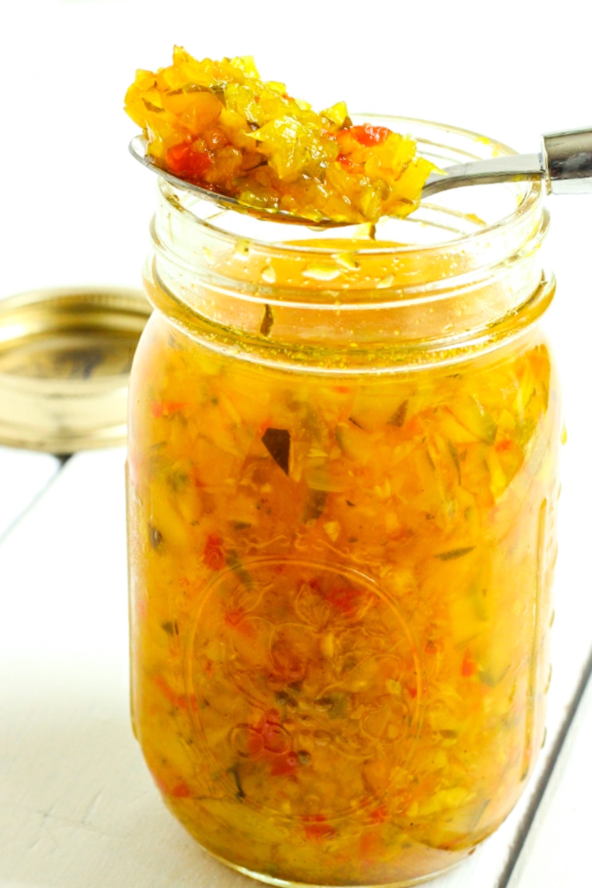 A jar of homemade zucchini relish, with a spoonful of relish resting on top of the open jar.