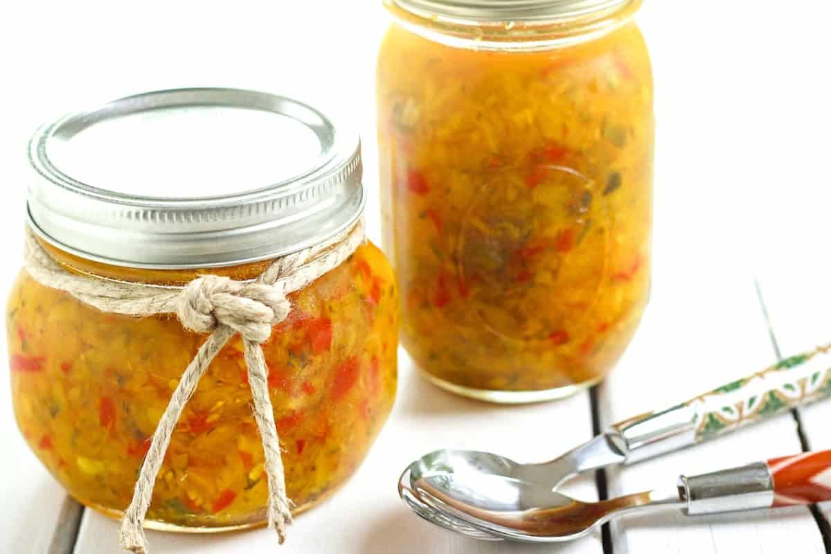 two jars of homemade zucchini relish with spoons lying next to the jars.