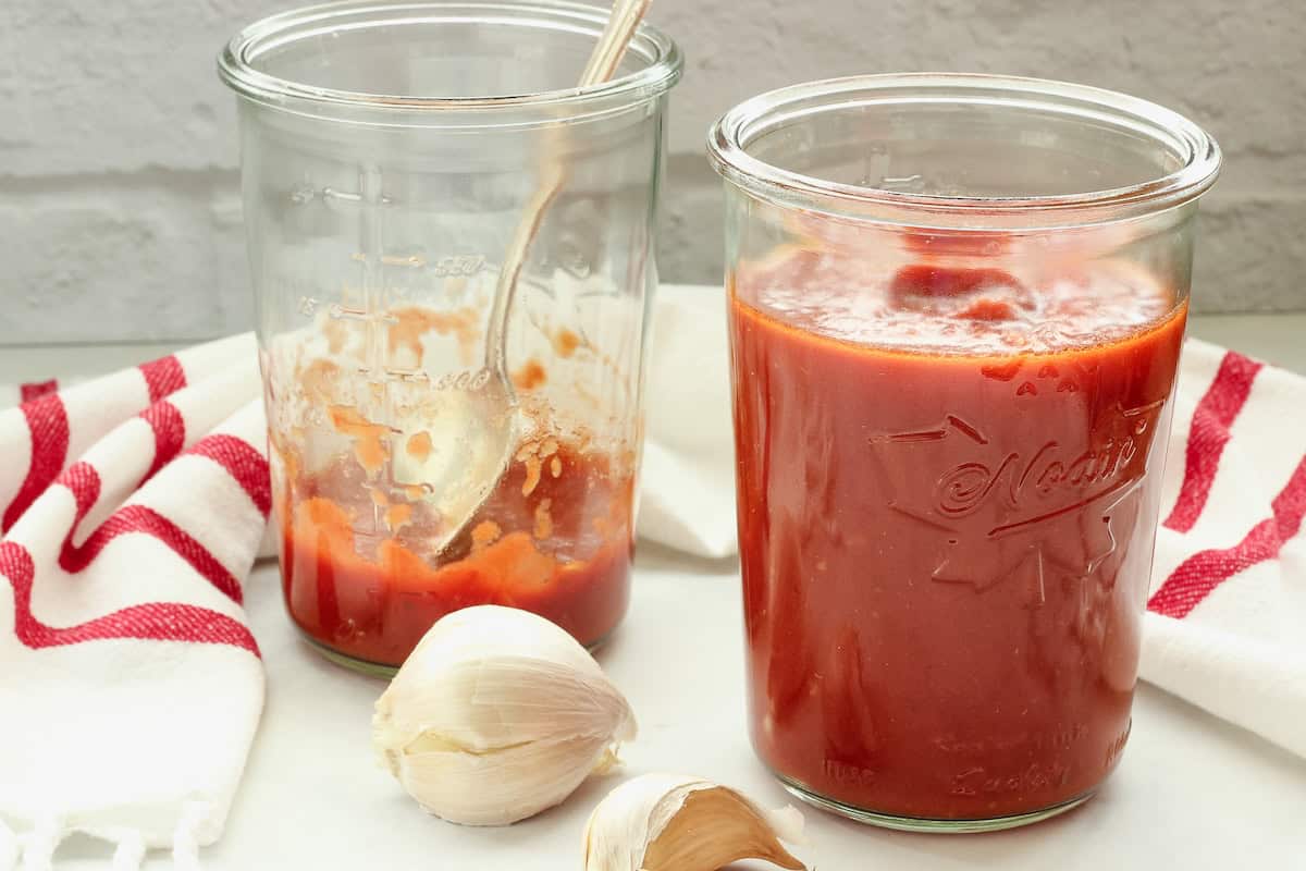 A full jar and a mostly empty jar of easy pasta sauce next to a red and white striped napkin and garlic bulbs.