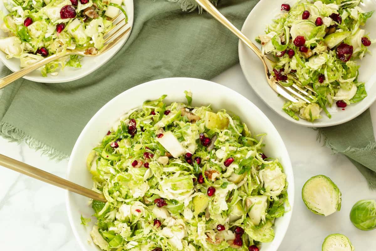 A large white serving bowl and 2 plates with shaved Brussels sprouts salad.