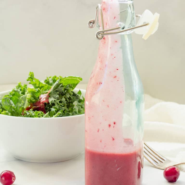 A bottle of homemade cranberry vinaigrette. A green salad in a white bowl is in the background.