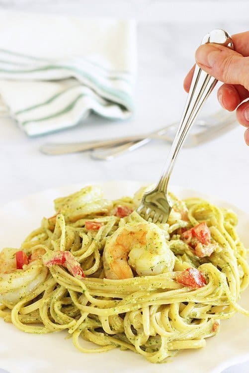 A plate of Fettuccine and Shrimp with Arugula Pesto Cream Sauce. A person is holding a fork in the pasta.