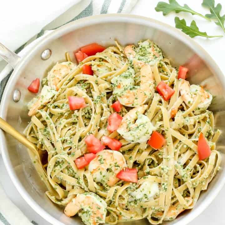 A pan of pasta with shrimp and pesto sauce on a white table.