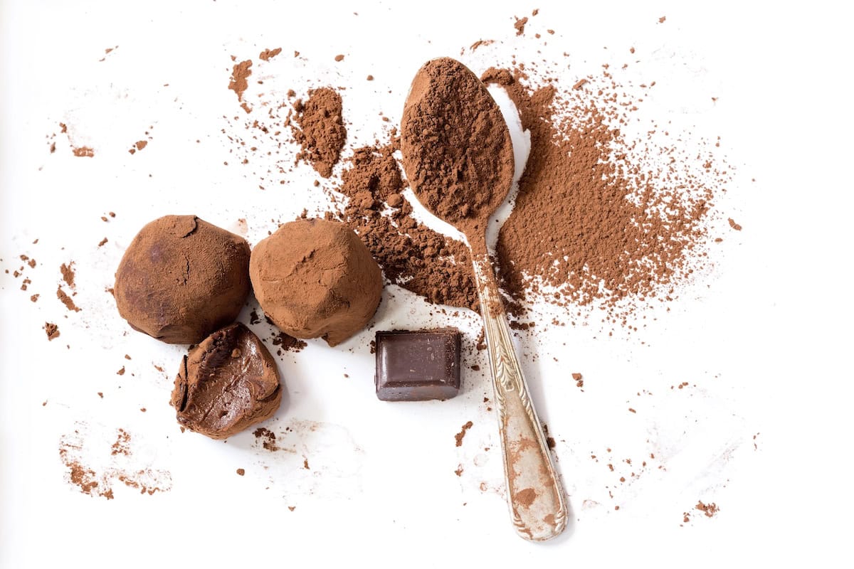 a spoon with cocoa powder and chocolate pieces on a white background.