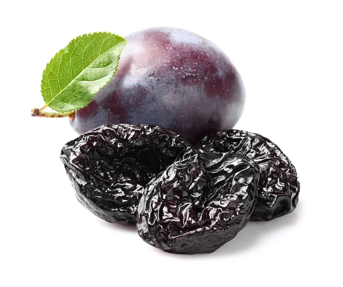 A plum with 3 dried prunes on a white background.