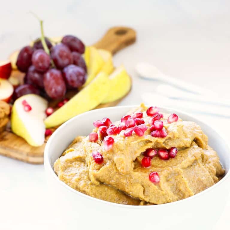 A bowl of pumpkin pie hummus alongside a board of fresh fruit.
