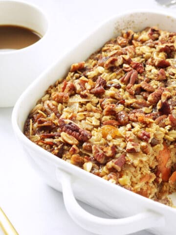 A casserole dish with carrot cake baked oatmeal and a cup of coffee in the background