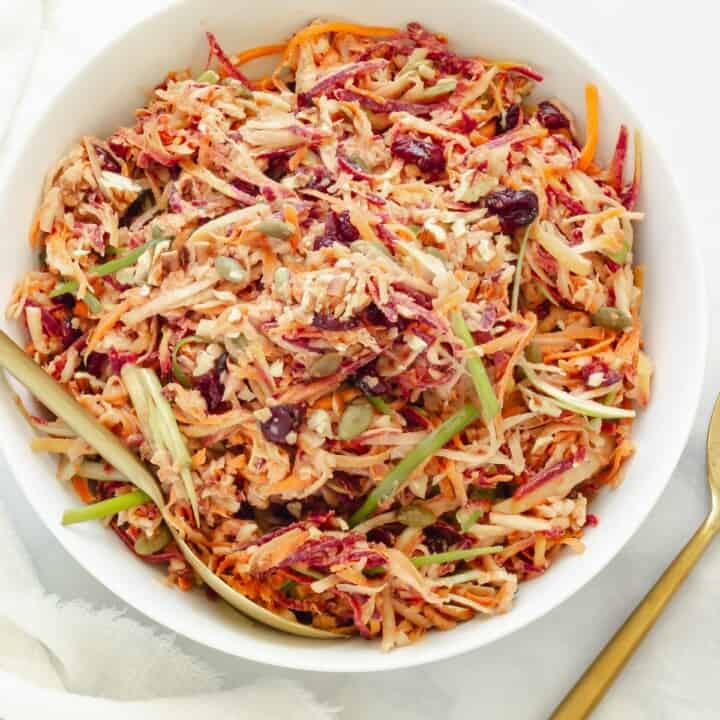 A white bowl of carrot slaw with gold servings spoons.