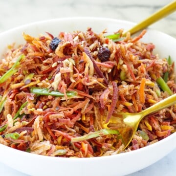 A white bowl of carrot slaw with two gold serving spoons.
