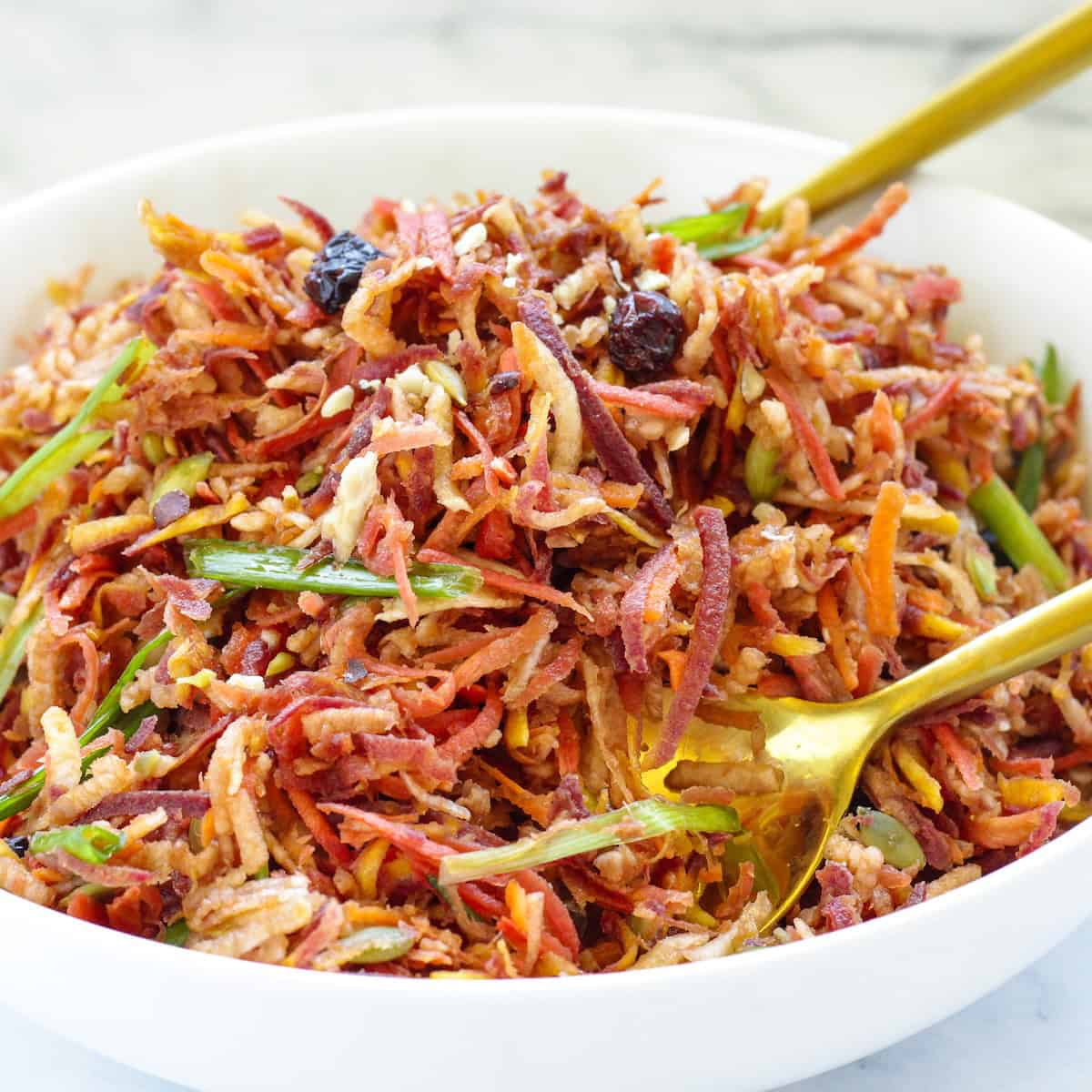 A white bowl of carrot slaw with two gold serving spoons.