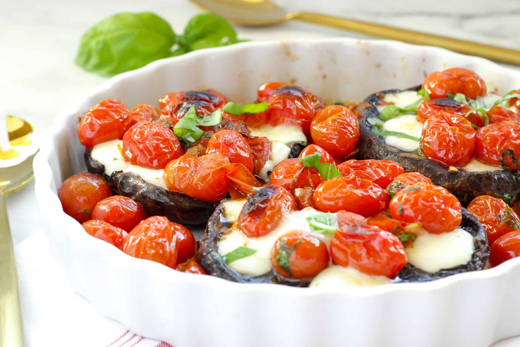 A white baking dish with Caprese stuffed Portobello mushroom caps - Portobellos stuffed with roasted tomatoes, mozzarella cheese, and herbs.