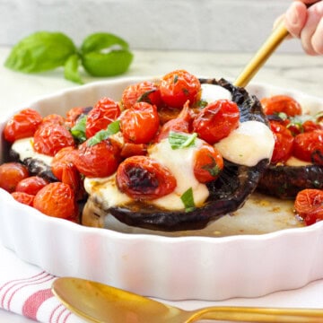 A gold serving spoon lifting a Caprese Stuffed Portobello Mushroom from a white casserole dish.