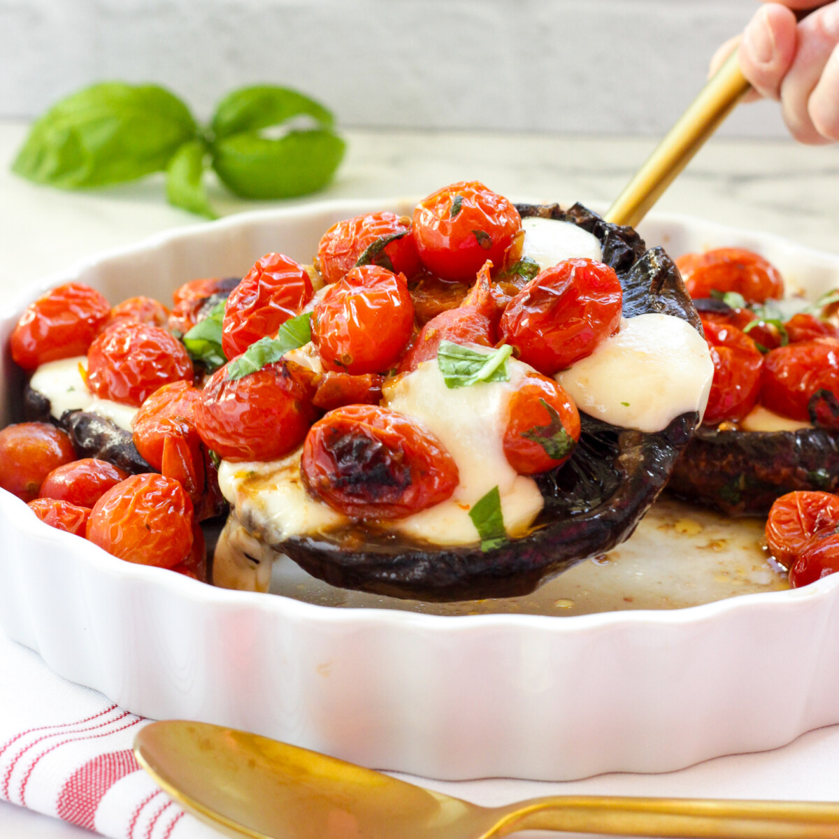 A gold serving spoon lifting a Caprese Stuffed Portobello Mushroom from a white casserole dish.