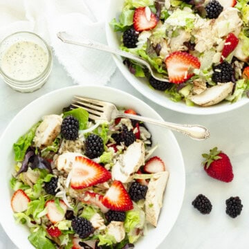 Two chicken and rice bowls with strawberries and blackberries. Some fresh berrier and a jar of salad dressing and next to the bowls.