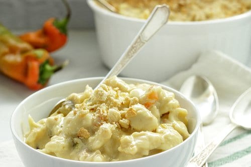 white bowl of mac and cheese with a casserole dish and Hatch chiles in the background