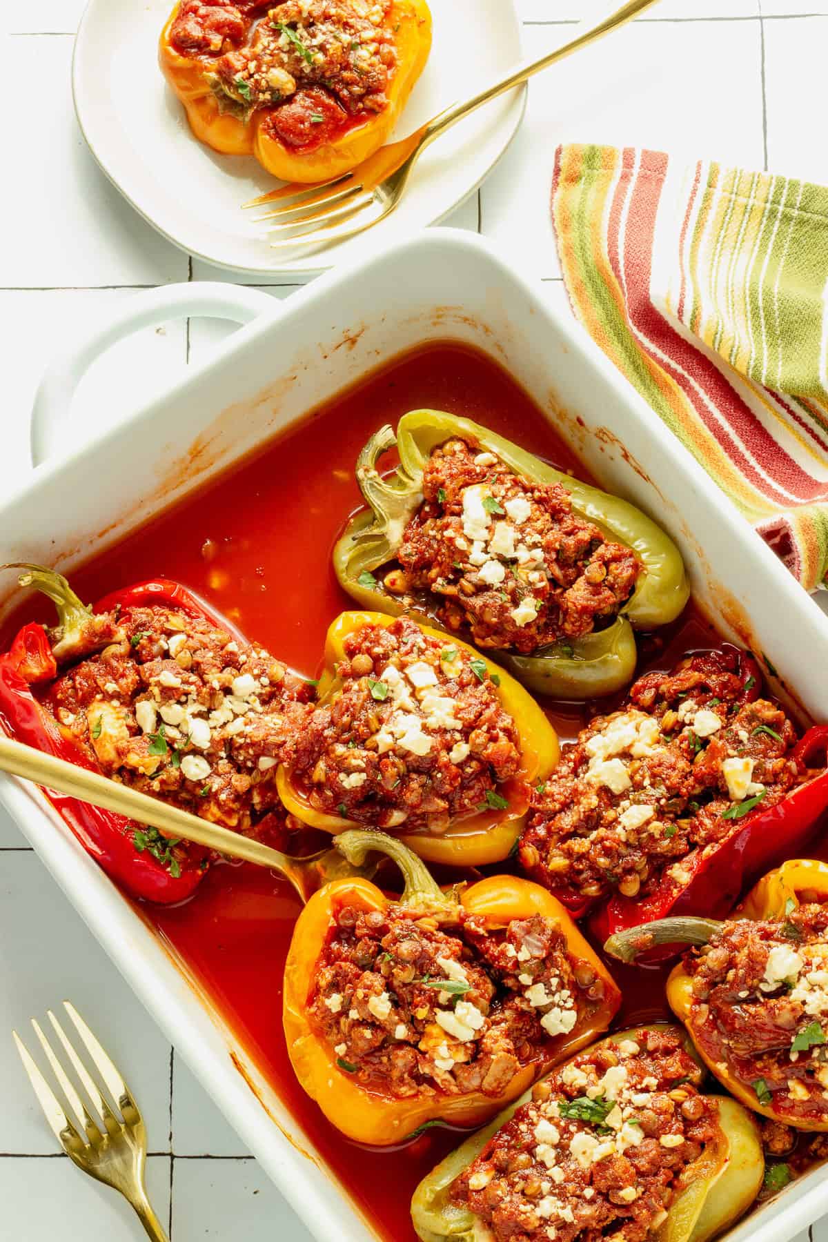 A white, rectangular casserole pan with ground turkey stuffed peppers. A red and green striped napkin and small plate with a stuffed pepper are next to the pan.