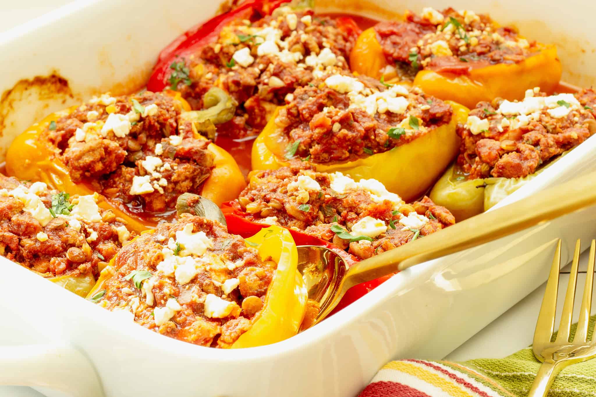 A white rectangular casserole pan filled with ground turkey stuffed peppers. A gold serving spoon is lifting one pepper from the pan.