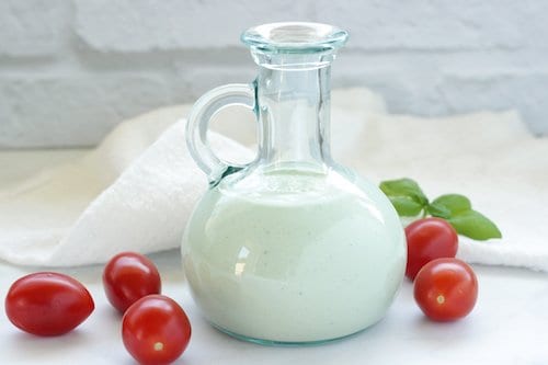 Salad dressing bottle with homemade blue cheese dressing surrounded by grape tomatoes and basil