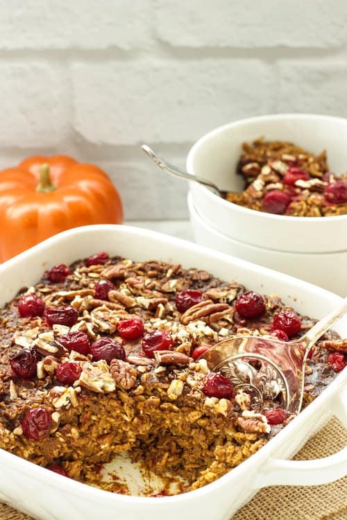 White casserole dish with pumpkin spice baked oatmeal topped with cranberries and pecans