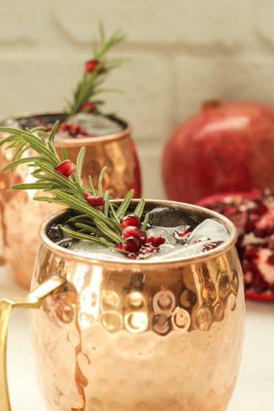 2 copper mugs with pomegranate mule cocktails garnished with a rosemary sprig and pomegranate arils