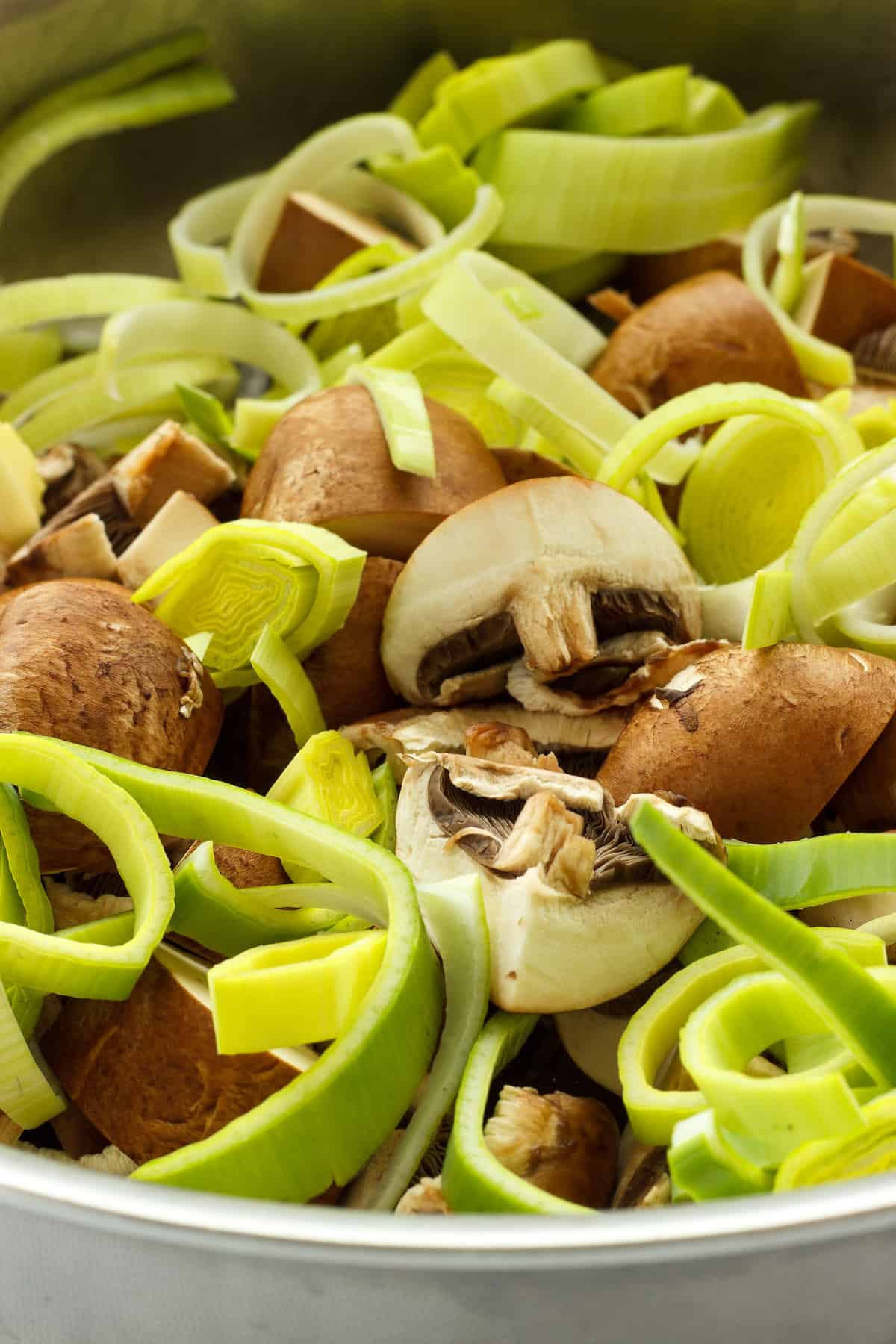 Instructions to make chicken with spinach and mushrooms. Sliced leeks and mushrooms cooking in a saute pan.