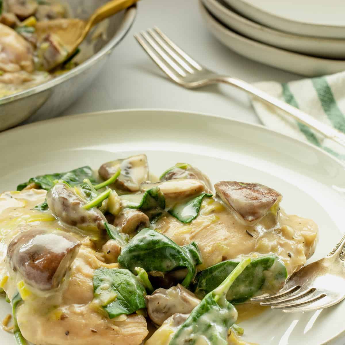 A white dinner plate and fork with chicken with spinach and mushrooms in a cream sauce.