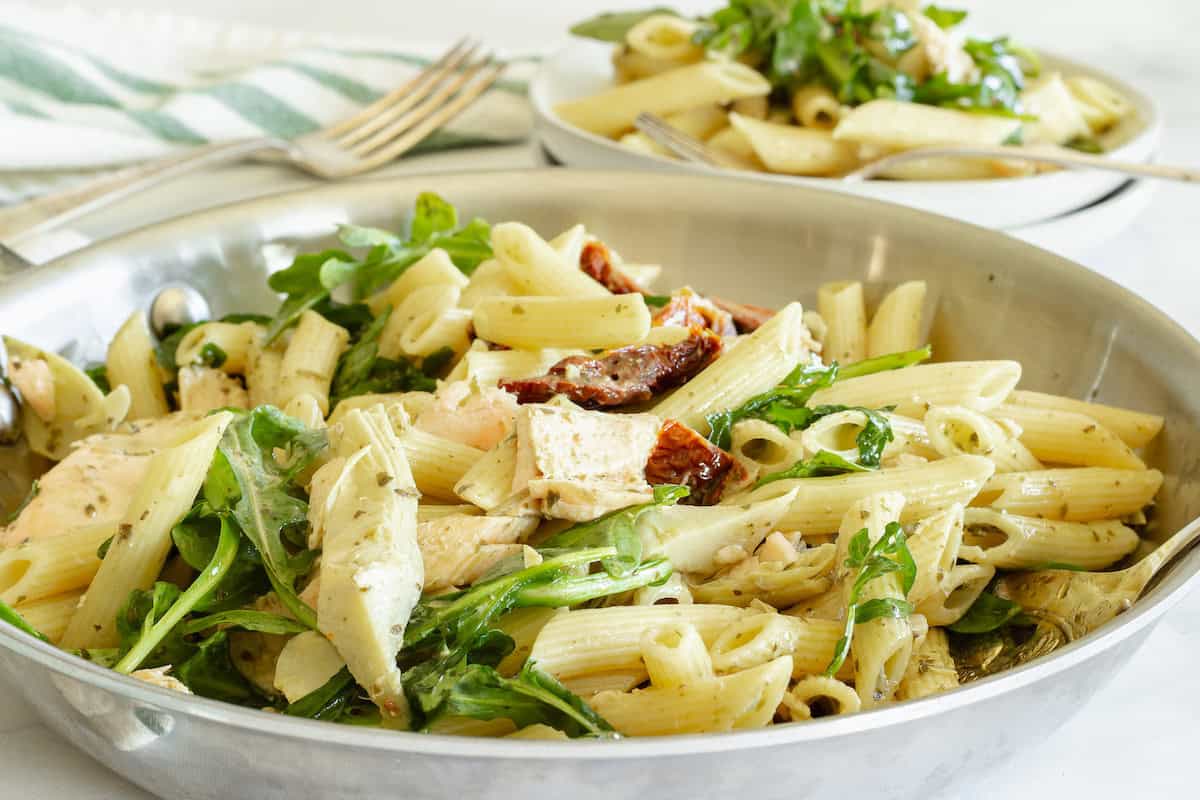 A pan of salmon pesto pasta with a green and white striped napkin in the background.