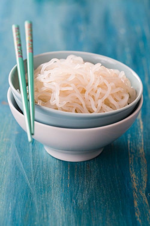 a white bowl of shirataki noodles on a blue background.