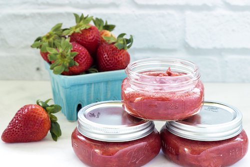 3 small jars of sugar-free strawberry rhubarb jam with a container of fresh strawberries in the background.