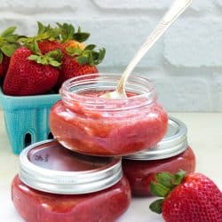 3 jars of strawberry rhubarb jam with a blue pint of fresh strawberries in the background