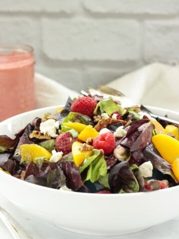 white bowl of salad topped with peaches and raspberries