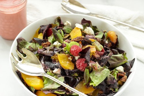 A large white bowl with a salad made with Peaches and Greens.