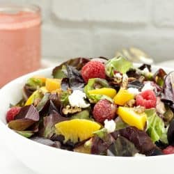 white bowl of salad topped with peaches and raspberries