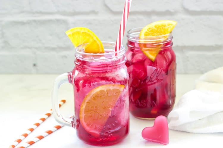 2 glasses of hibiscus green iced tea with orange slices and striped straws