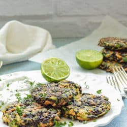 white plate with 3 vegetable fritters and a half of a lime